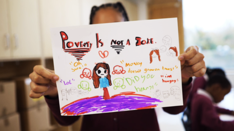 A child holding a drawing that reads "poverty is not a joke"
