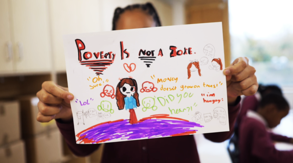 A child holding a drawing that reads "poverty is not a joke"